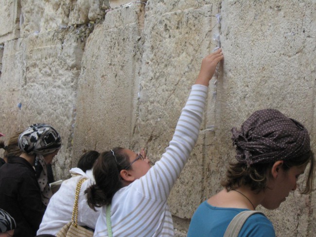 Девушка кладет записку в щель Стены Плача в Иерусалиме.